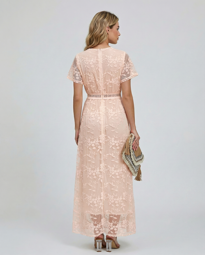 Female model showcasing a floral maxi dress with long sheer sleeves against a plain background.