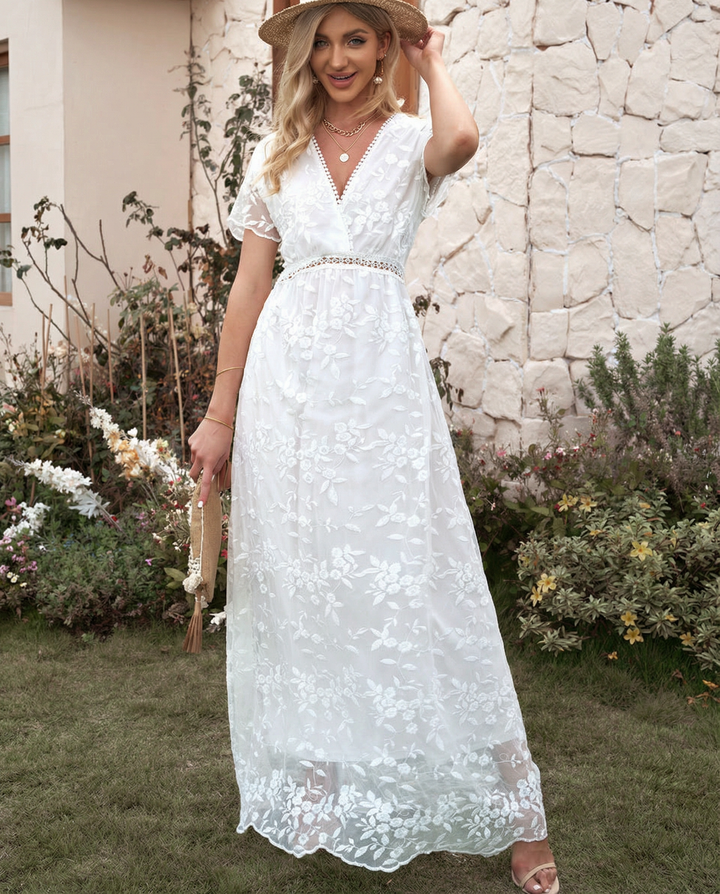 Female model in a formal floral maxi dress with sheer long sleeves on a plain background.
