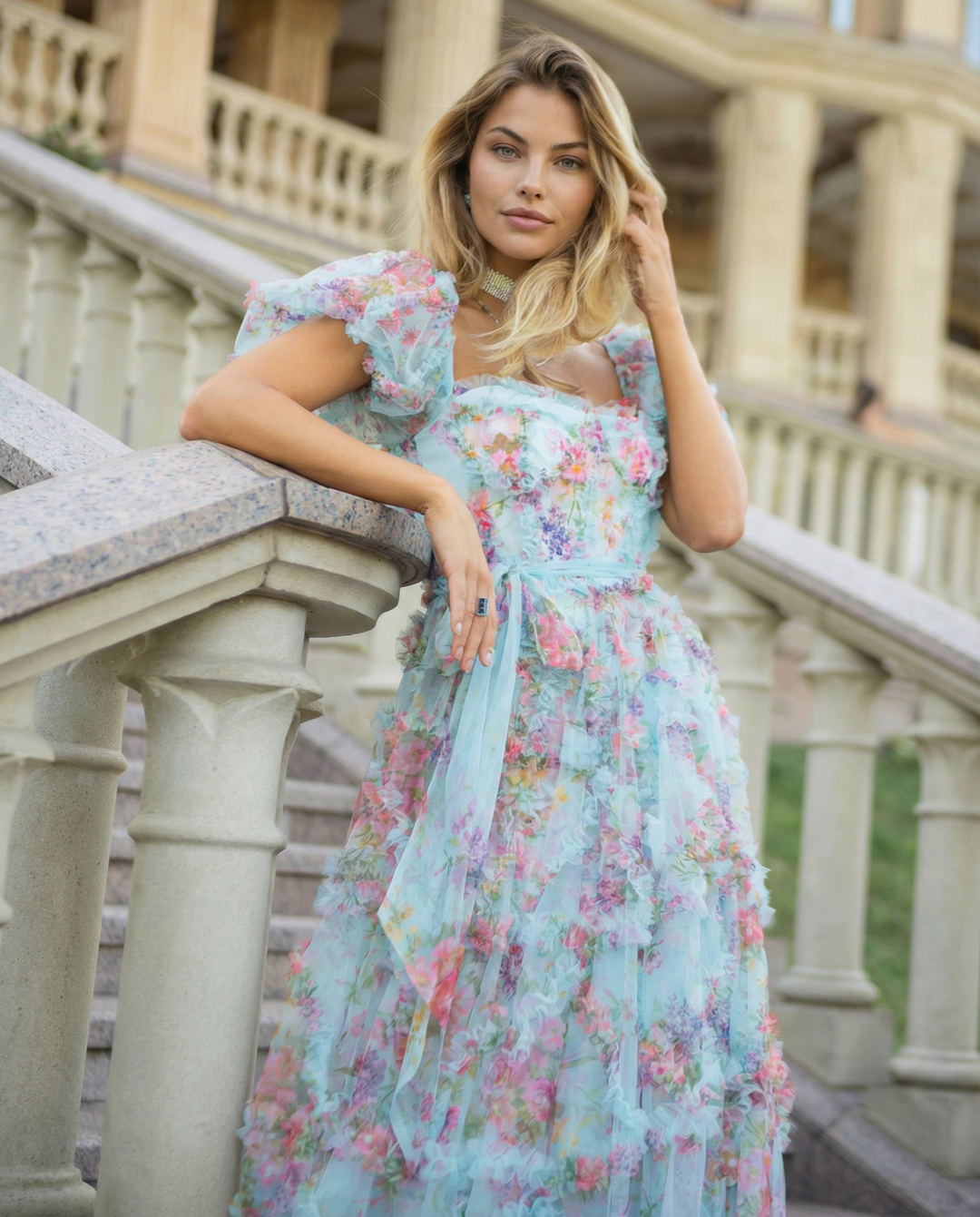 Woman wearing a floral maxi dress with layered skirt and bow waist detail.