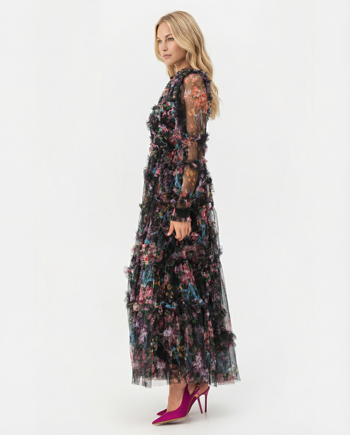 Model wearing a long floral ruffle dress with sheer sleeves on a plain background.