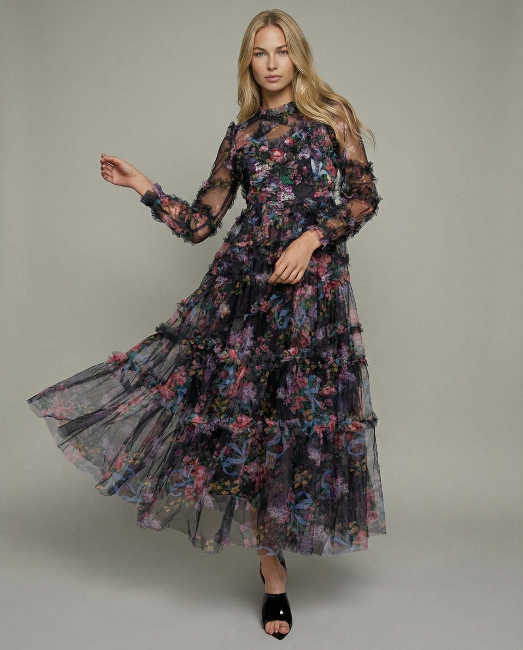 Female model in a black tiered maxi dress with floral detailing on a plain background.