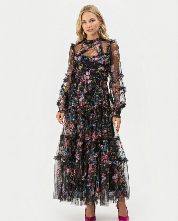 Female model wearing a floral tiered maxi dress with sheer long sleeves on a plain background.
