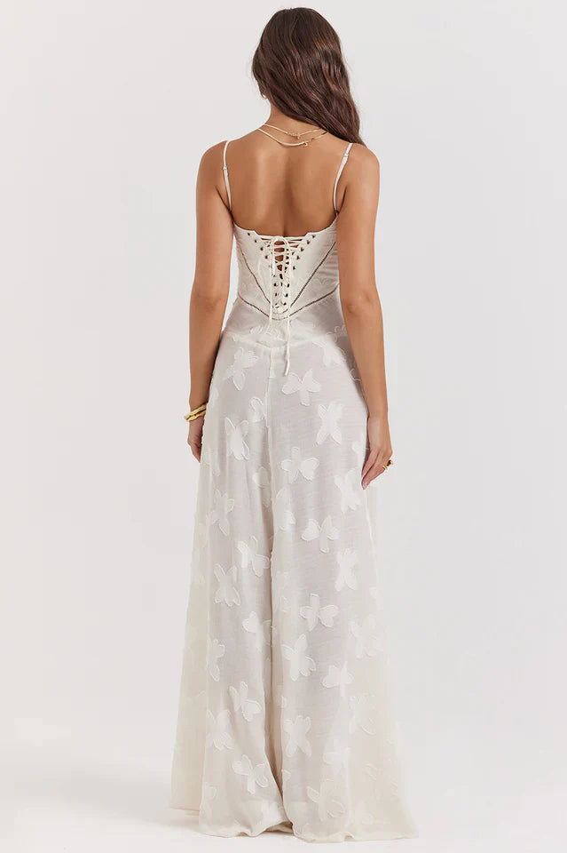 Woman in a cream floral maxi dress with a flowing skirt on a plain background.