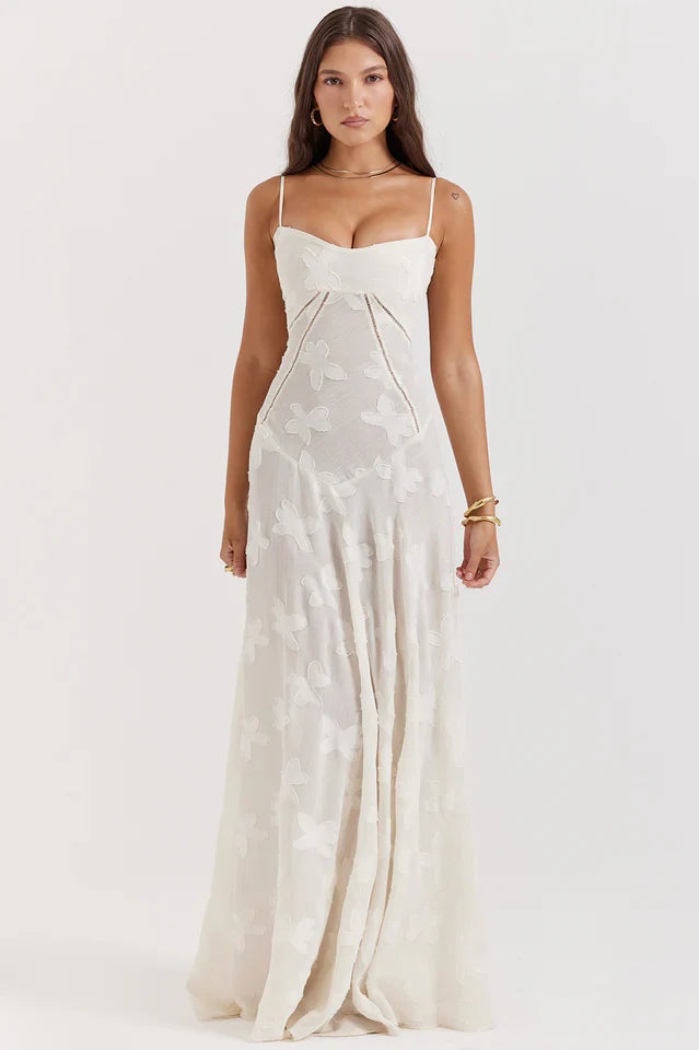 Female model wearing a floral maxi dress with slim straps on a plain background.