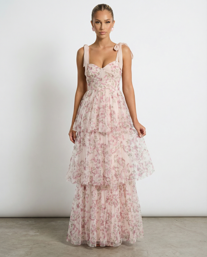 Female model wearing a white floral maxi dress with tie-up straps on a plain background.