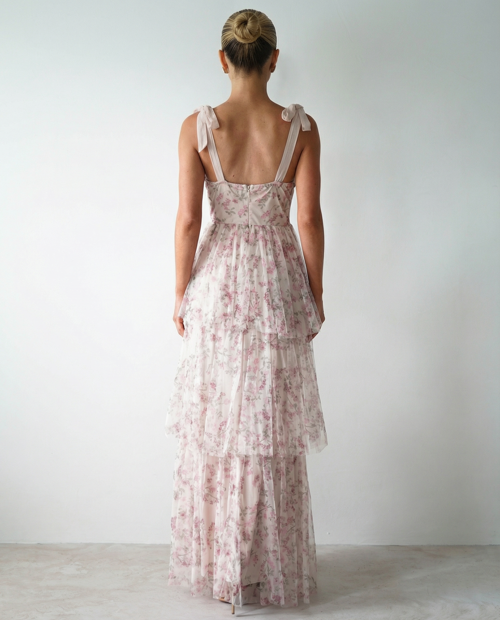 Woman in a white tiered maxi dress with floral print on a plain background.
