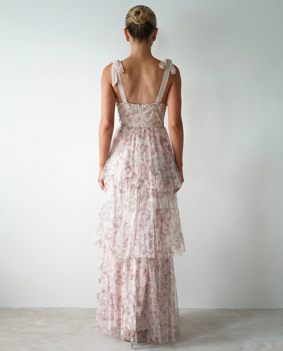 Woman in a white tiered maxi dress with floral print on a plain background.