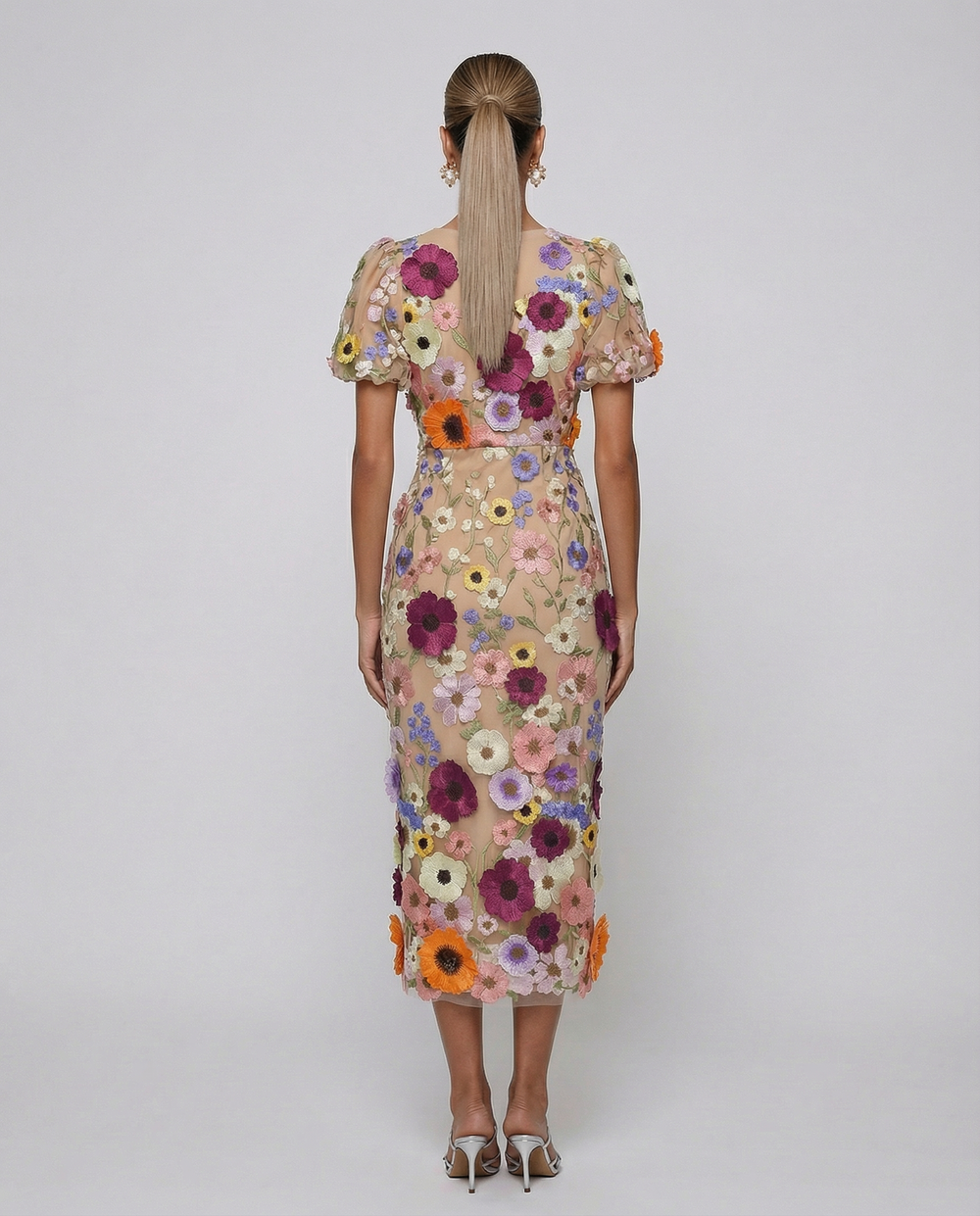 Woman in a V neckline midi dress with floral detailing on a plain background.
