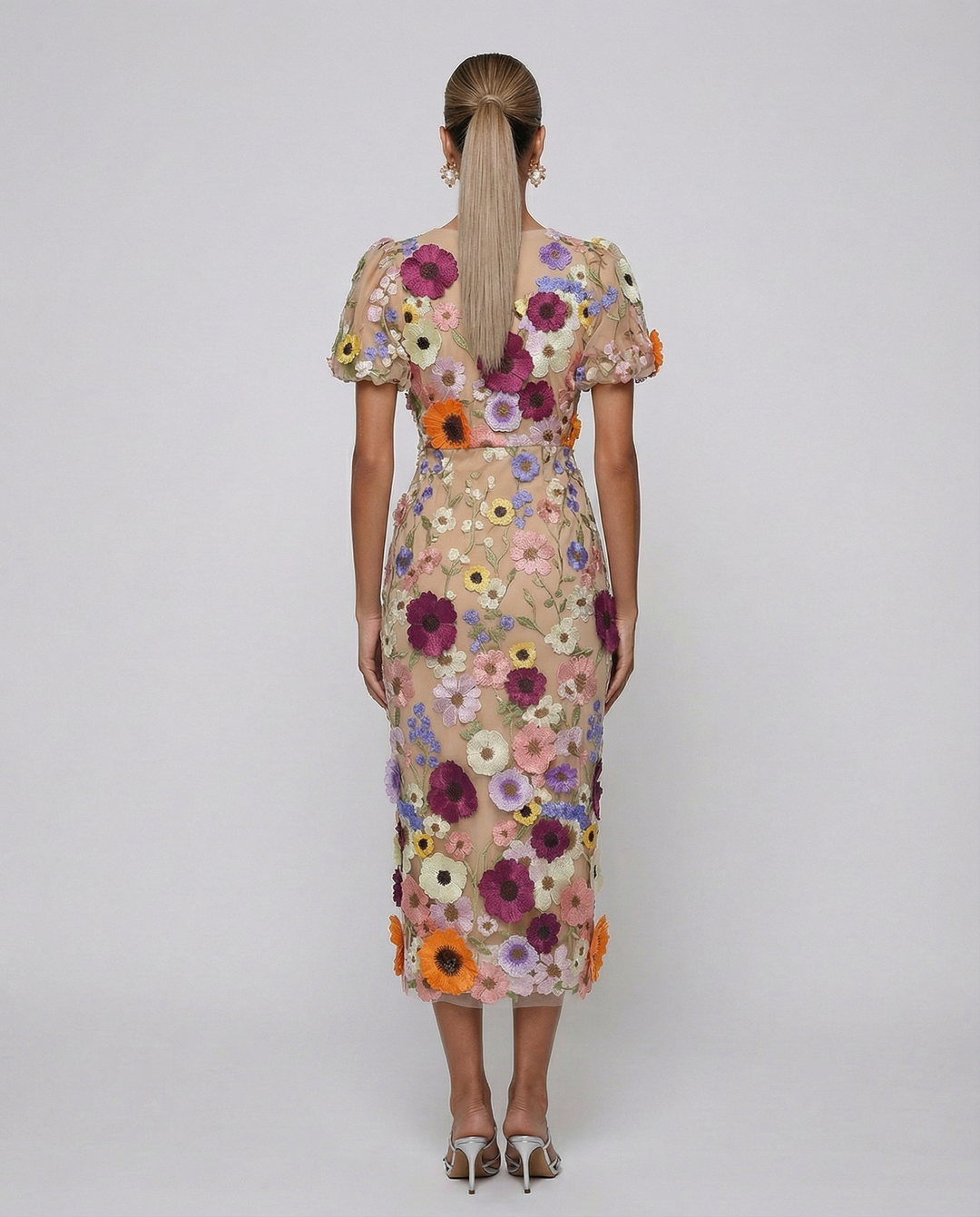 Woman in a V neckline midi dress with floral detailing on a plain background.