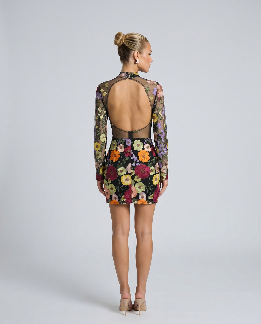 Woman in a fitted long sleeve embroidered mini dress on a plain background.