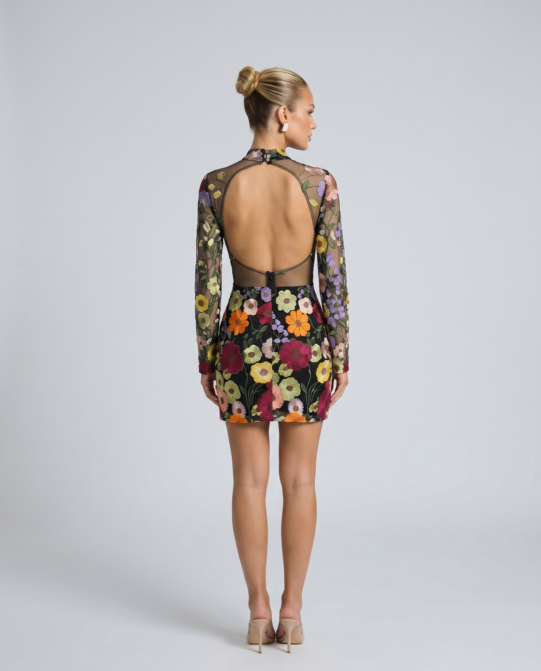 Woman in a fitted long sleeve embroidered mini dress on a plain background.