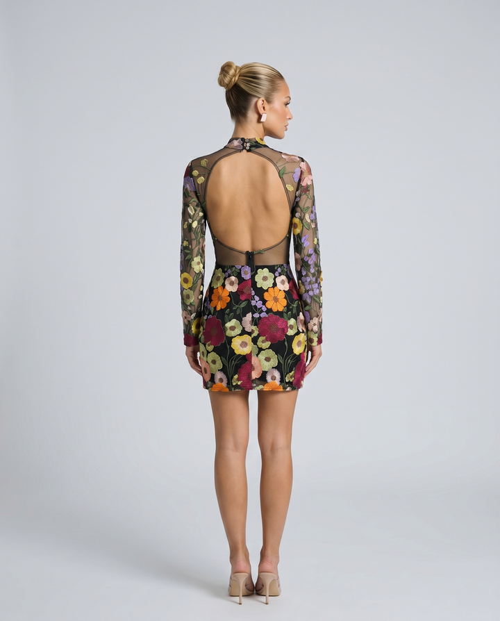 Woman in a fitted long sleeve embroidered mini dress on a plain background.