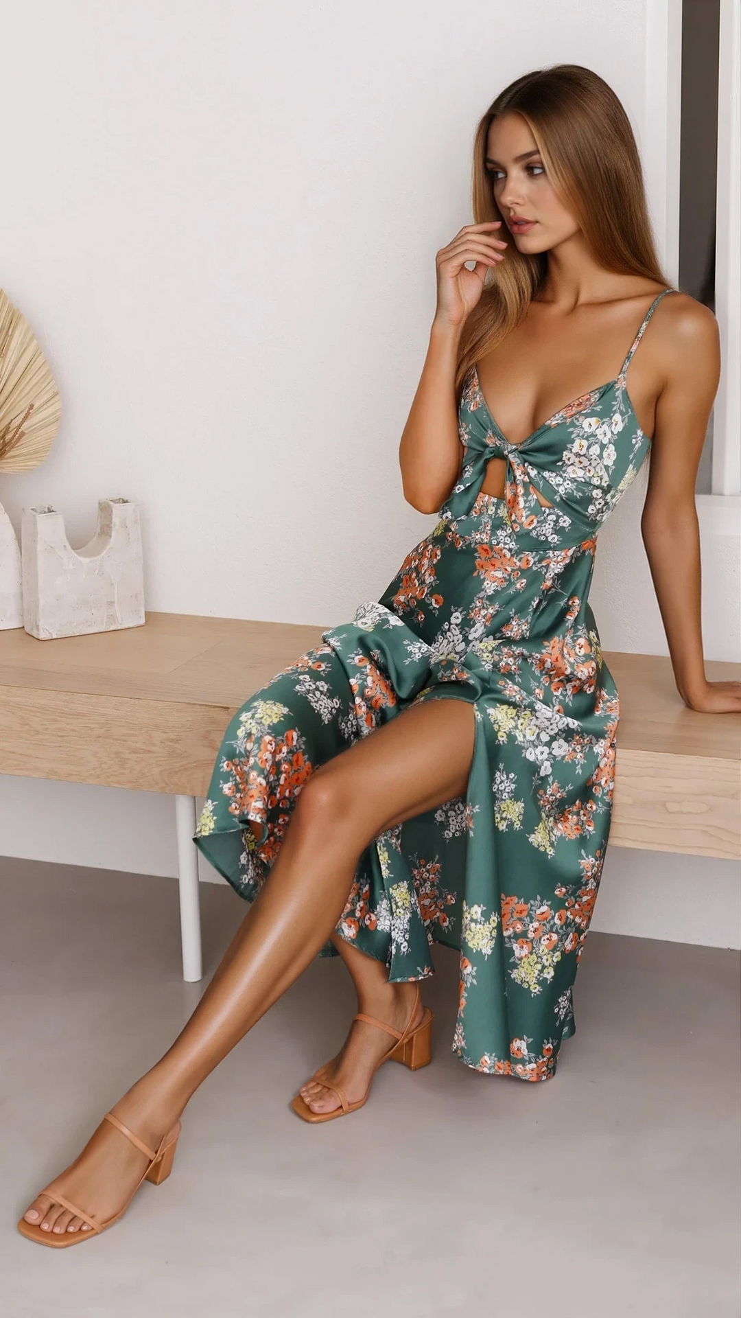 Woman wearing a green floral midi dress with adjustable straps against a plain background.
