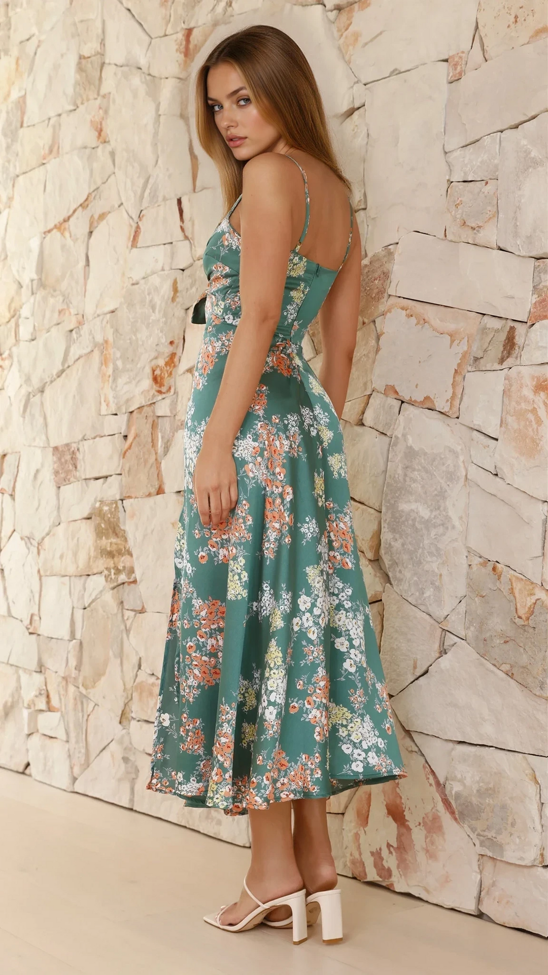 Woman styled in a green floral midi dress with flowing skirt on a wall background.