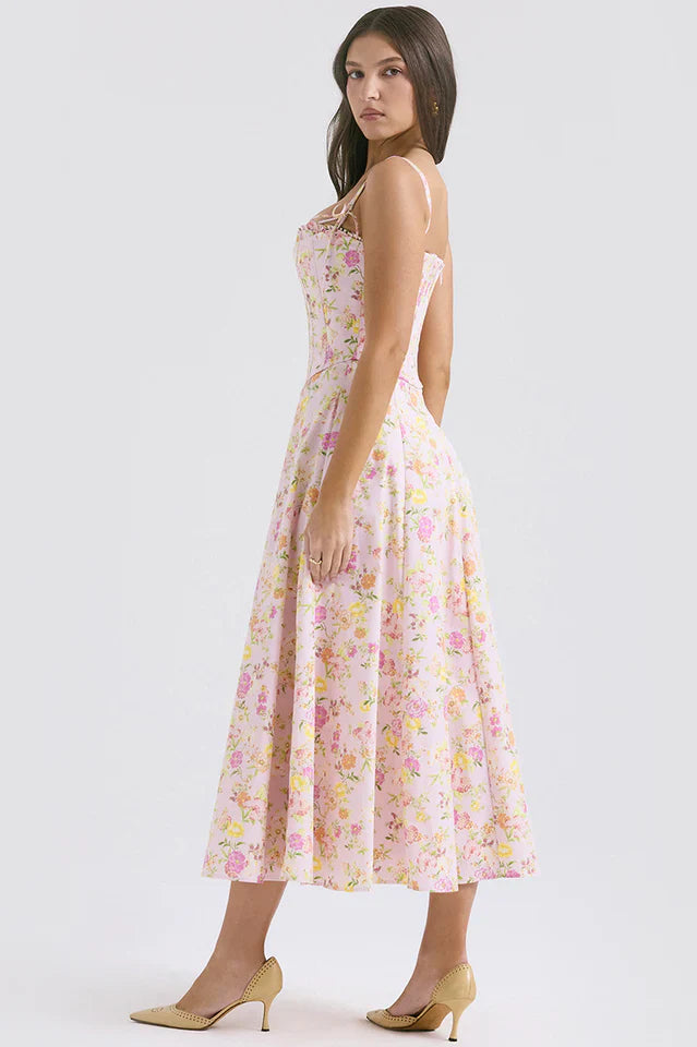 Woman showcasing a sleeveless pink floral midi dress with a flowing skirt on a plain background.