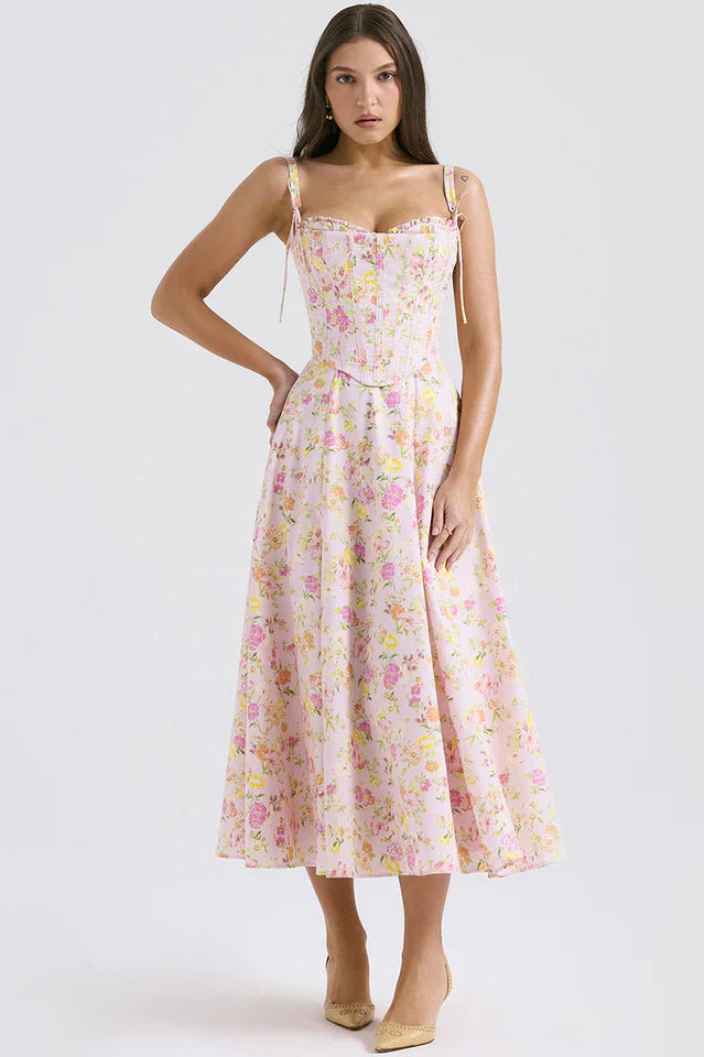 Woman wearing a pink floral midi dress with straps against a plain background.