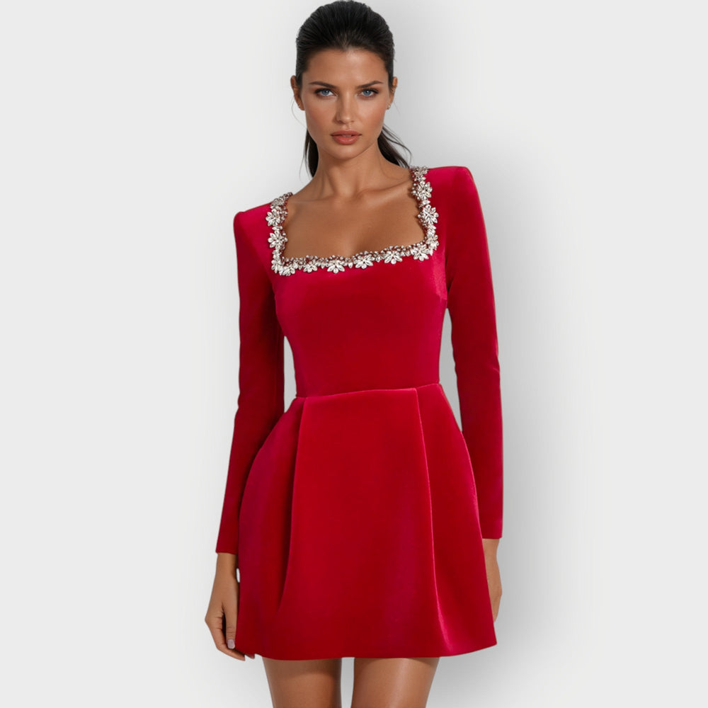 Woman posing in a fitted velvet mini dress with elegant evening styling on a plain backdrop.