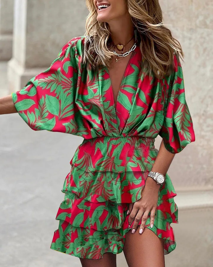 Woman posing in a deep V-neck mini dress with layered ruffle details on a plain backdrop.