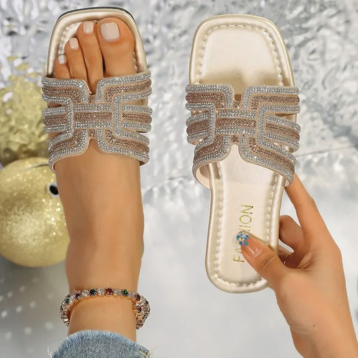 Women’s open-toe slide sandals with dazzling crystal details on a plain background.
