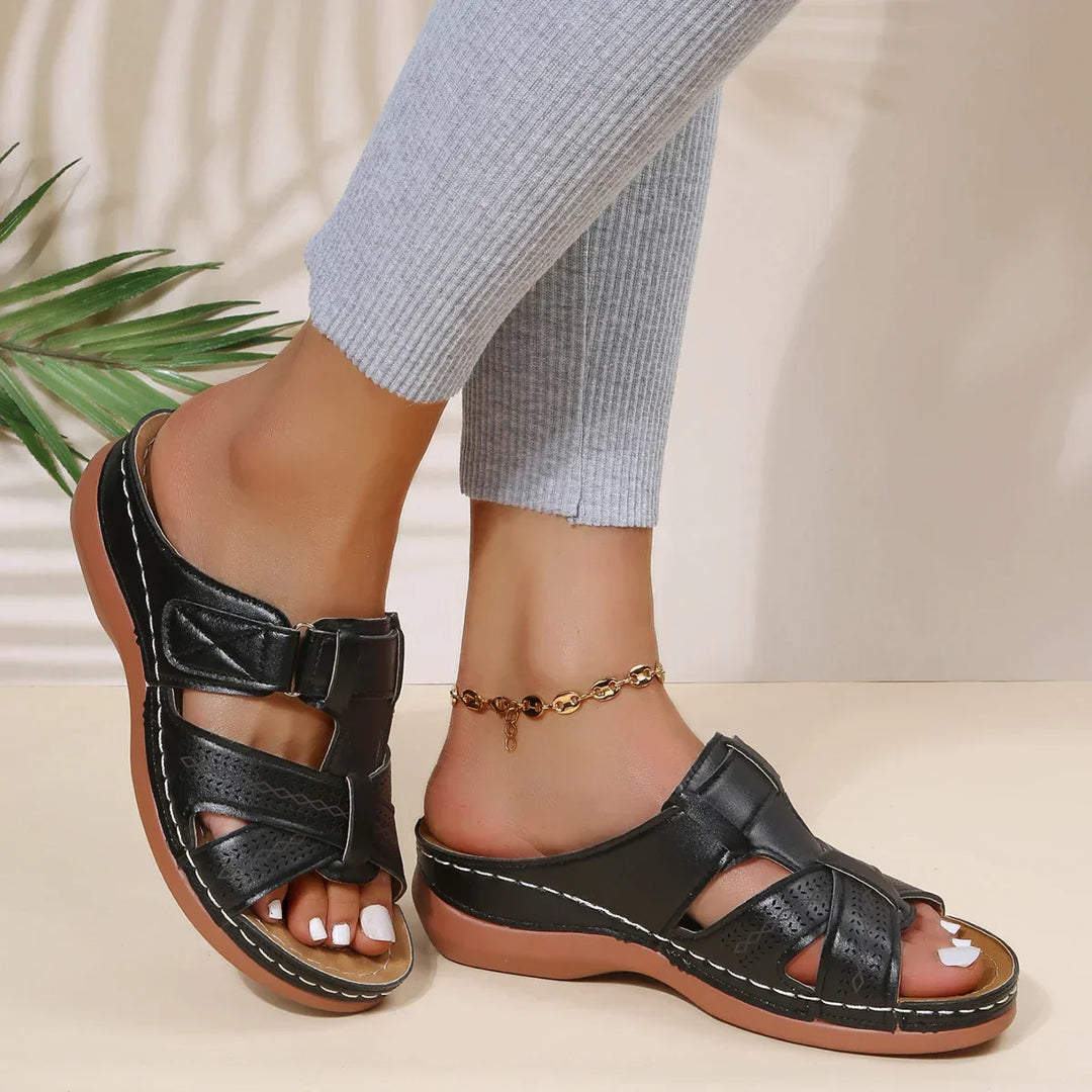 Woman standing in stylish wedge sandals against a plain background.