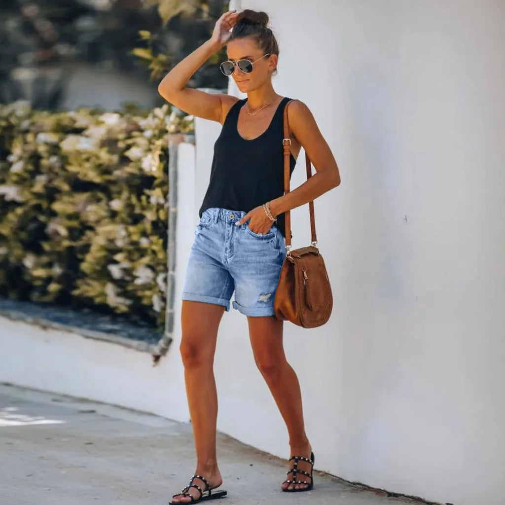 Female model wearing high waist distressed denim shorts with rolled hem against a plain background.