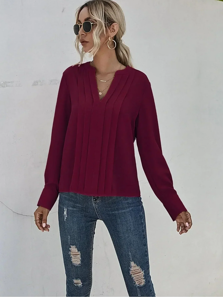 Airy draped blouse with elegant pleats worn by a person on a clean background.