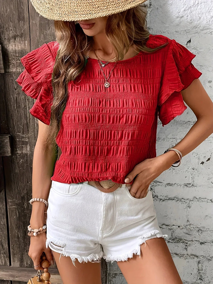 model wearing a relaxed airy blouse with playful ruffles against a plain background.