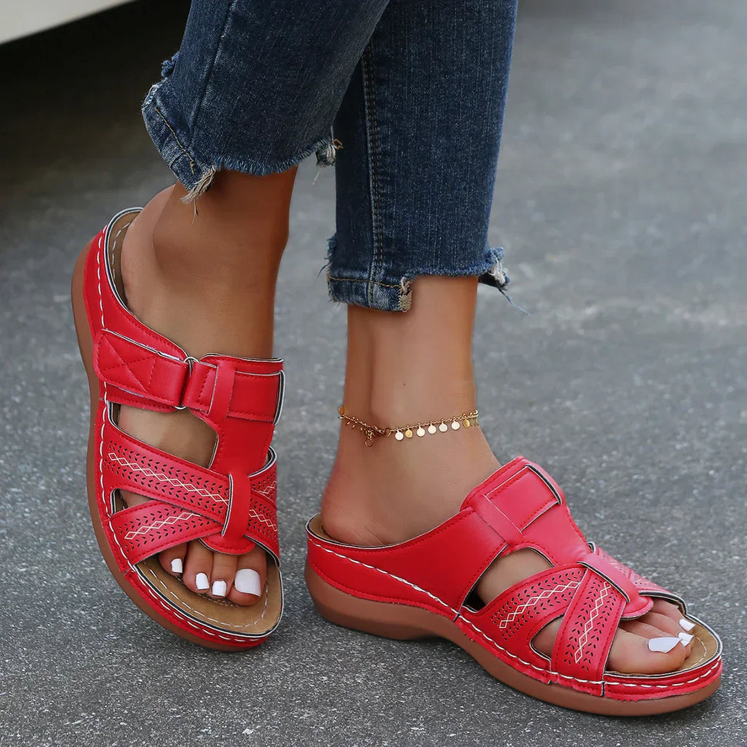 Woman wearing open-toe wedge sandals with a clean plain backdrop.