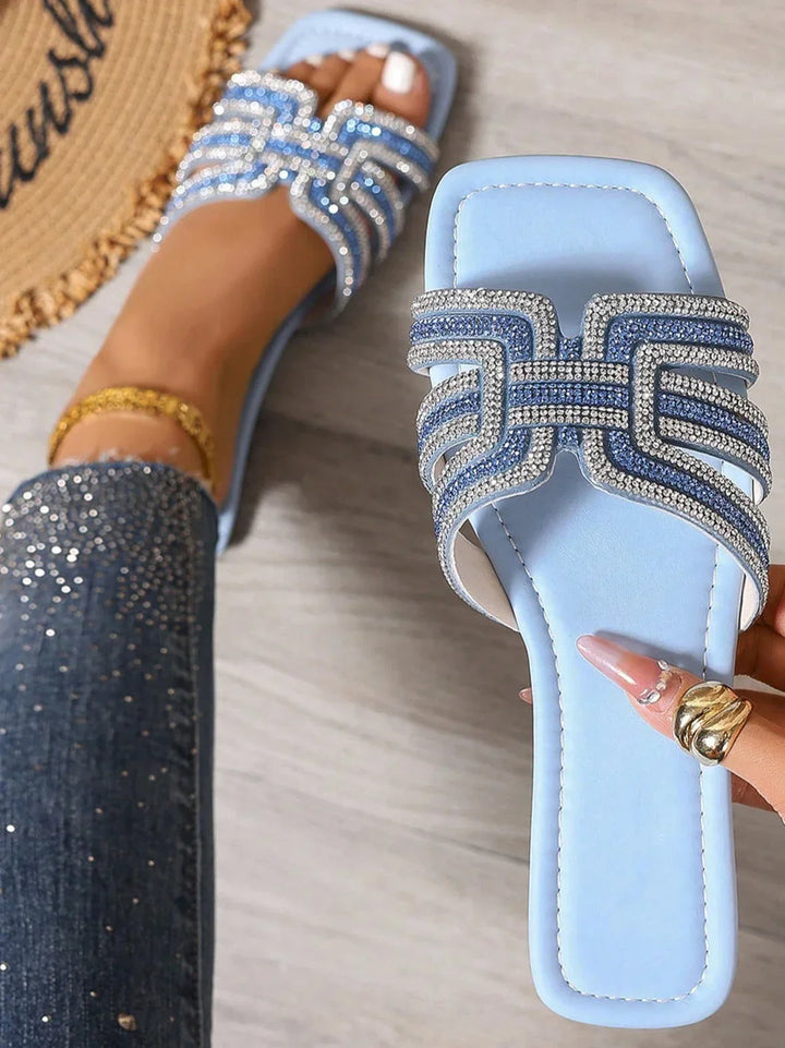 Sparkling women’s flat sandals displayed on a simple plain background.
