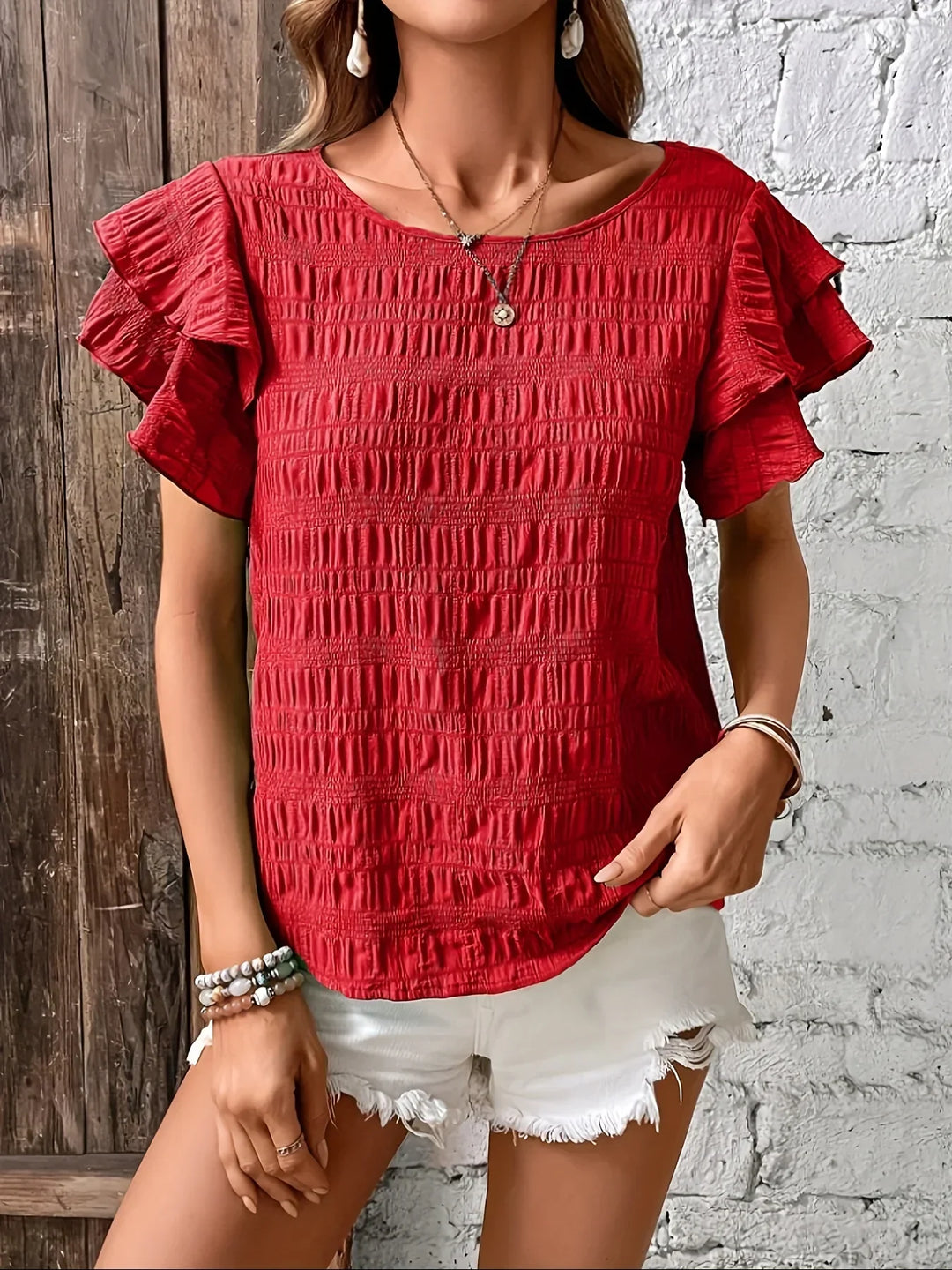 Woman showcasing a feminine blouse with graceful movement against a block wall background.