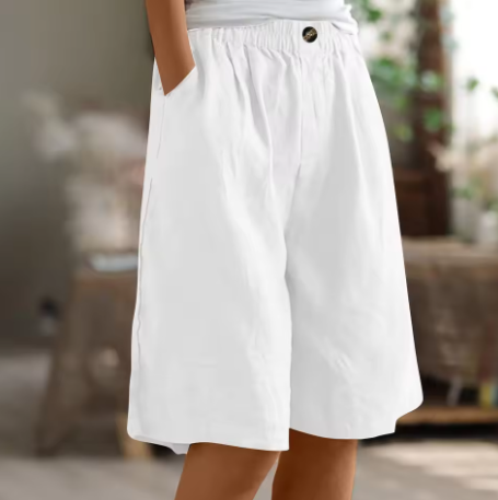 Woman showcasing soft draped shorts with simple styling on a plain background.