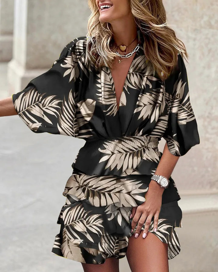 Female posing in a bright patterned dress with ruffle skirt and relaxed fit on a plain backdrop.