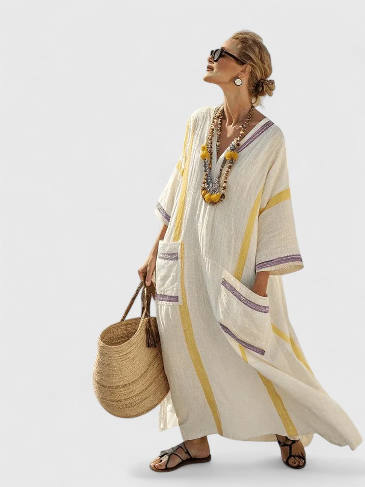 Female model wearing a flowing V-neck kaftan dress with patch pockets on a plain background.