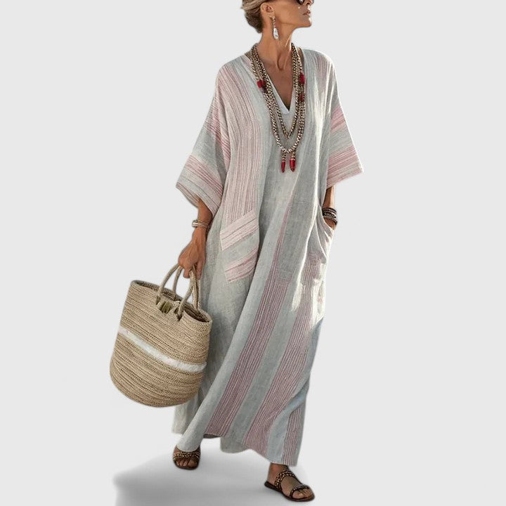 Flowing striped maxi dress on a plain background with front pockets and casual warm-weather style.