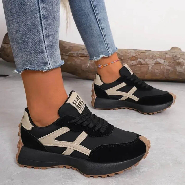 Female model wearing cushioned walking sneakers on a plain background.