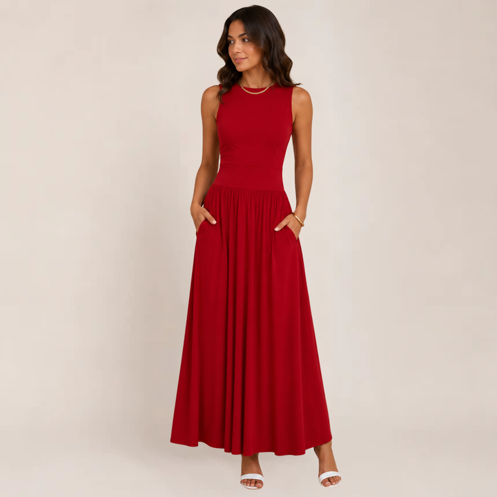 Woman posing in a flowing sleeveless formal maxi dress against a plain background.