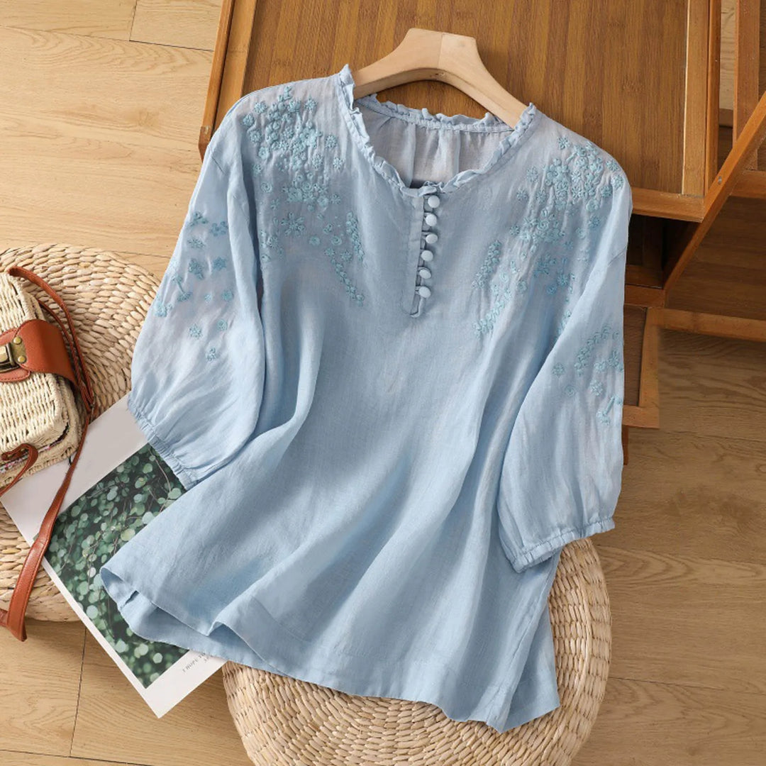 Elegant feminine blouse with delicate embroidery on a plain background.