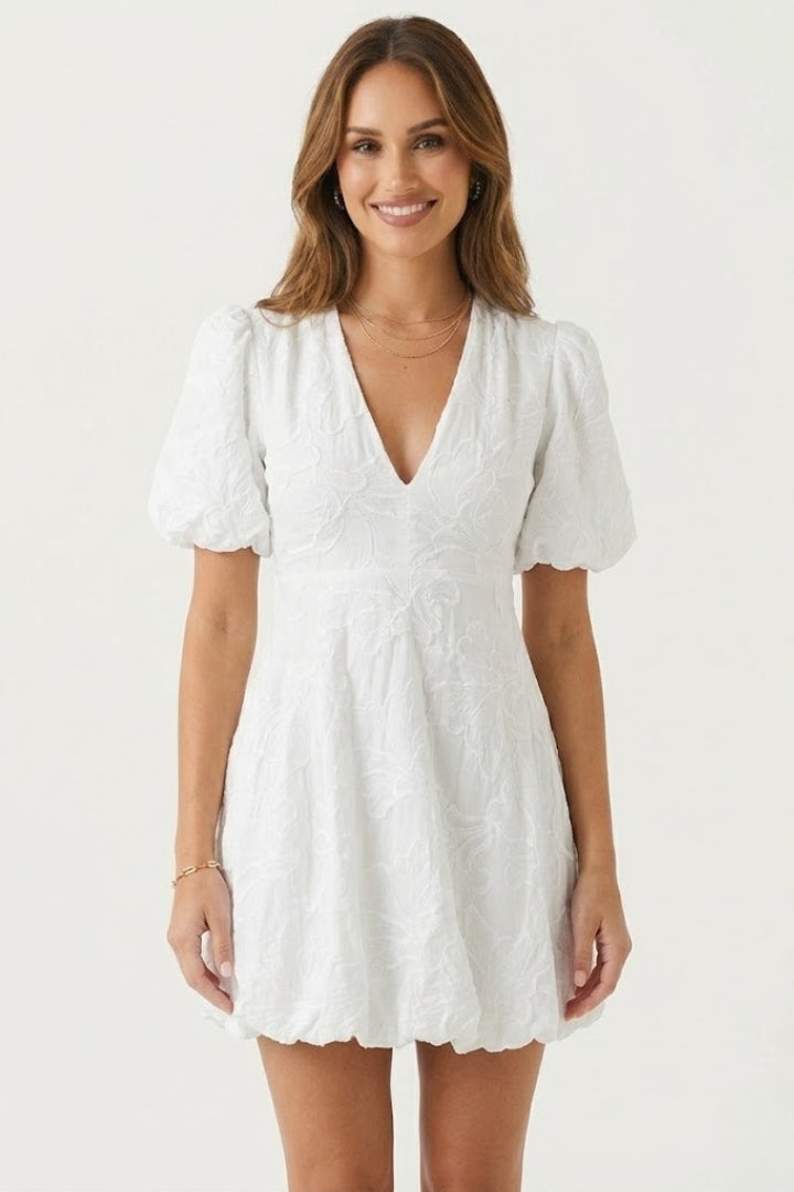 Woman wearing embroidered mini dress with puff sleeves on gray background.