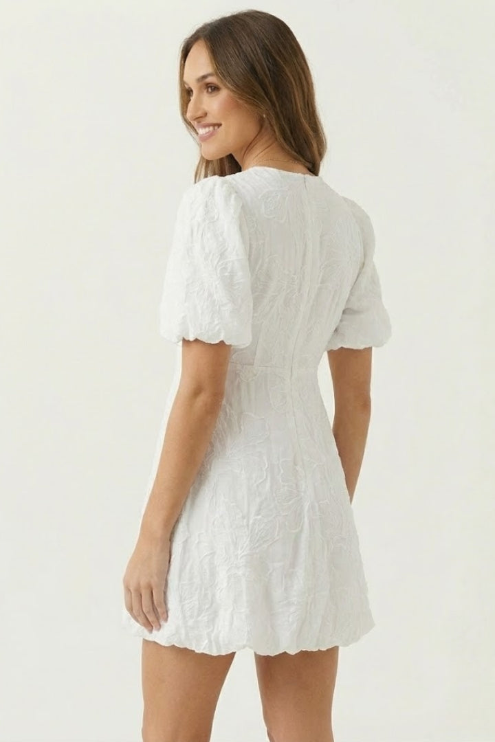 Woman showing back angle of embroidered dress on gray backdrop.