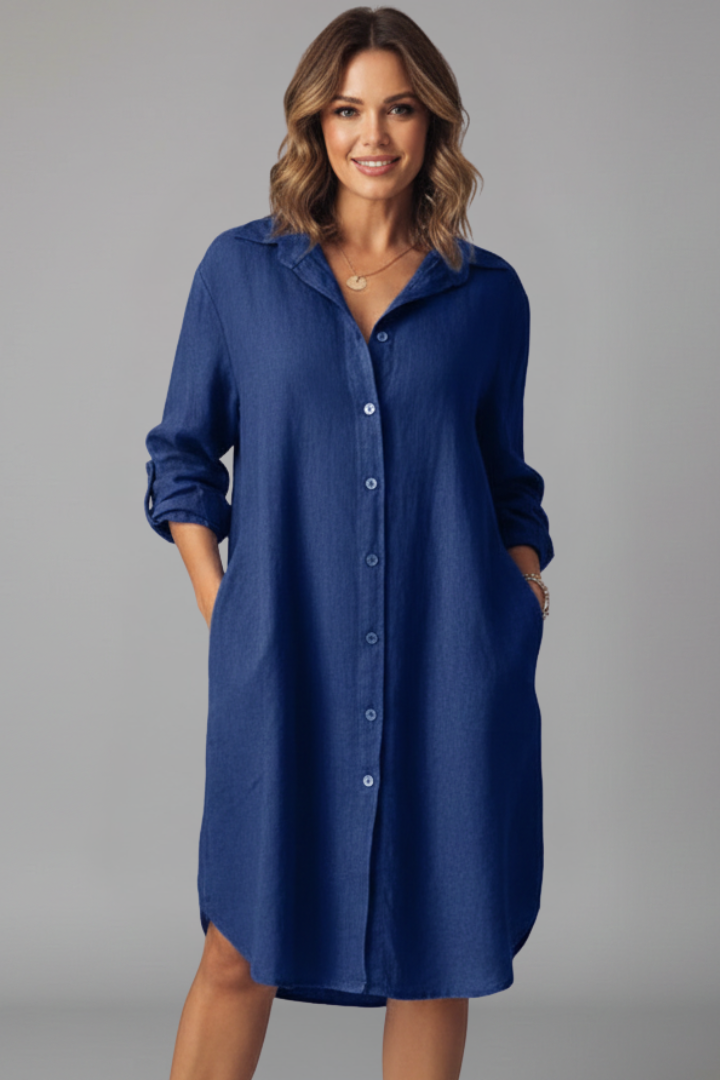  Female model in a button-down shirt dress with a short hem on a plain background.