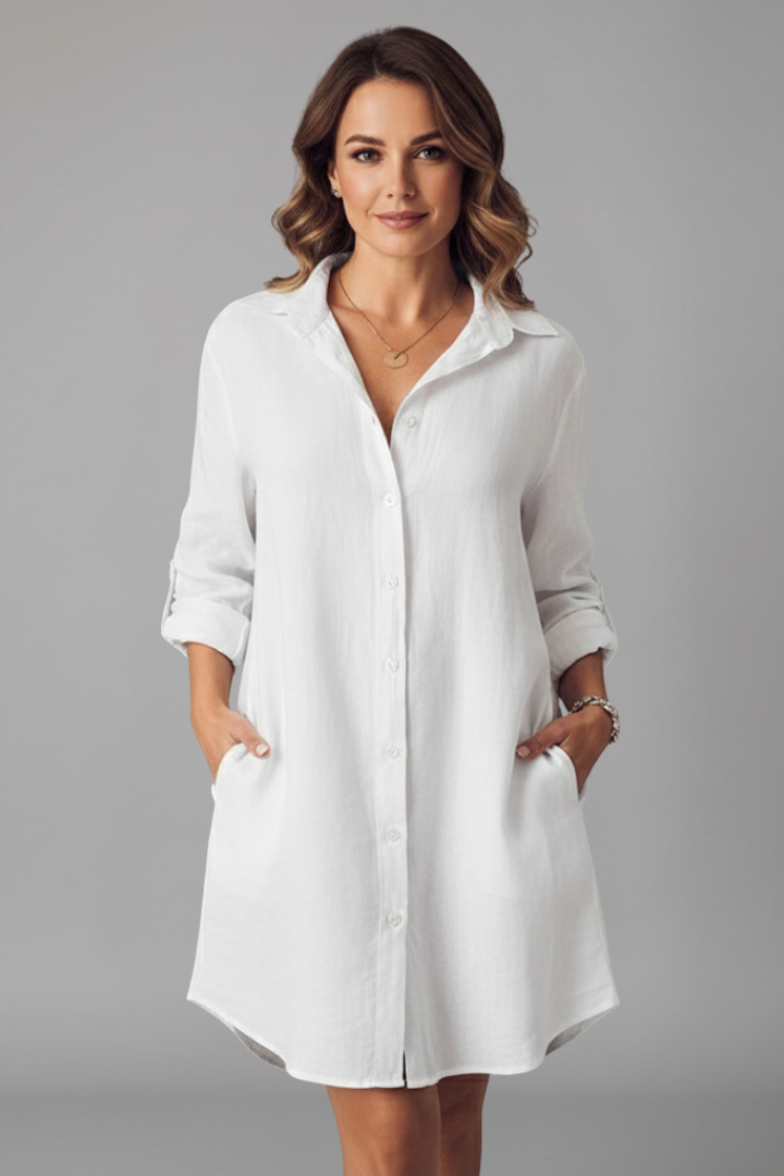  Woman wearing a short shirt dress with a classic collar and button closure against a plain background.