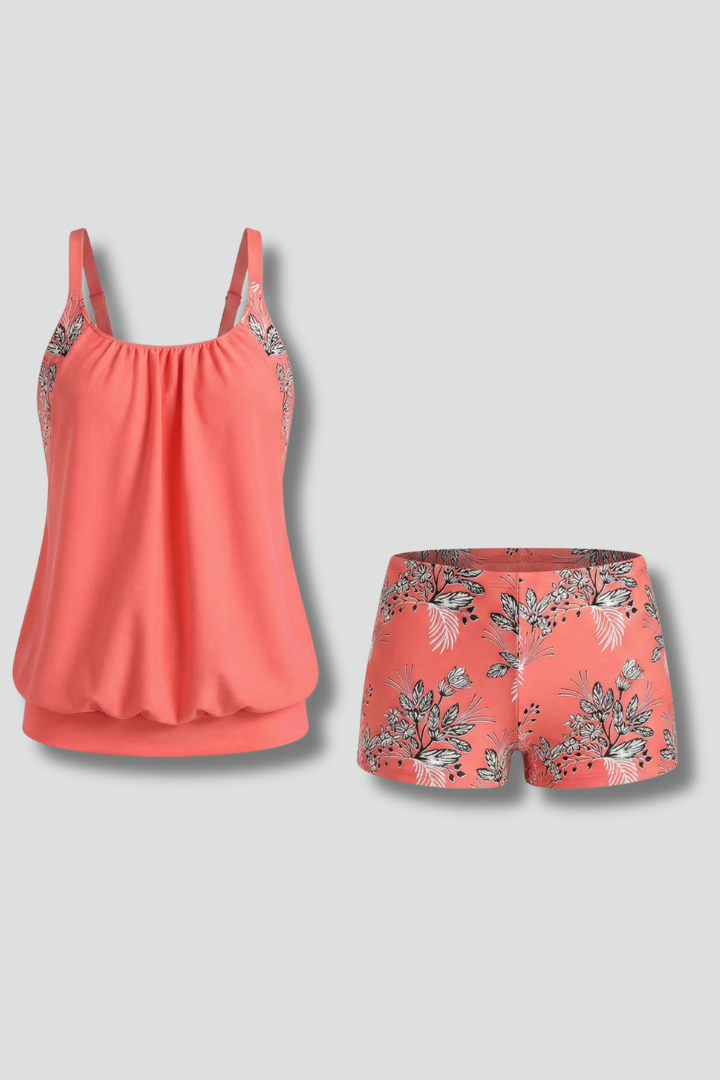 Woman wearing floral tankini set with shorts on plain gray background.