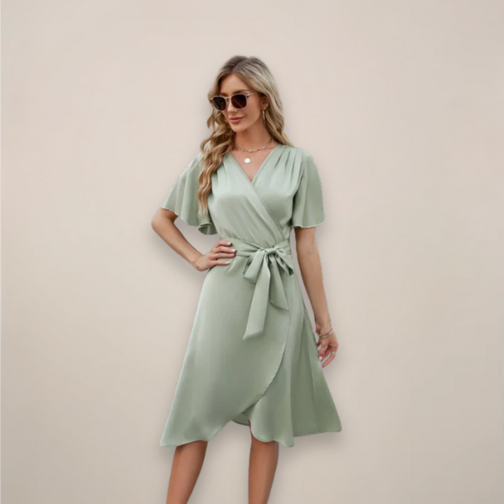 Woman in a wrap-style midi dress featuring short sleeves and a tie detail on a plain background.
