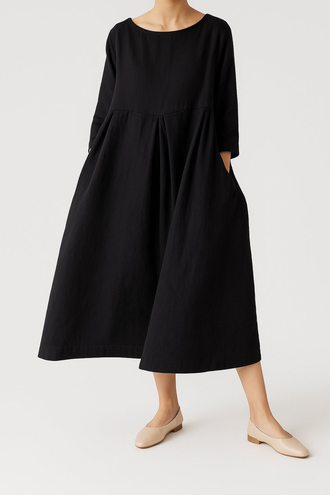 Woman dressed in a wide-cut midi dress with soft front pleat detail on a plain background.