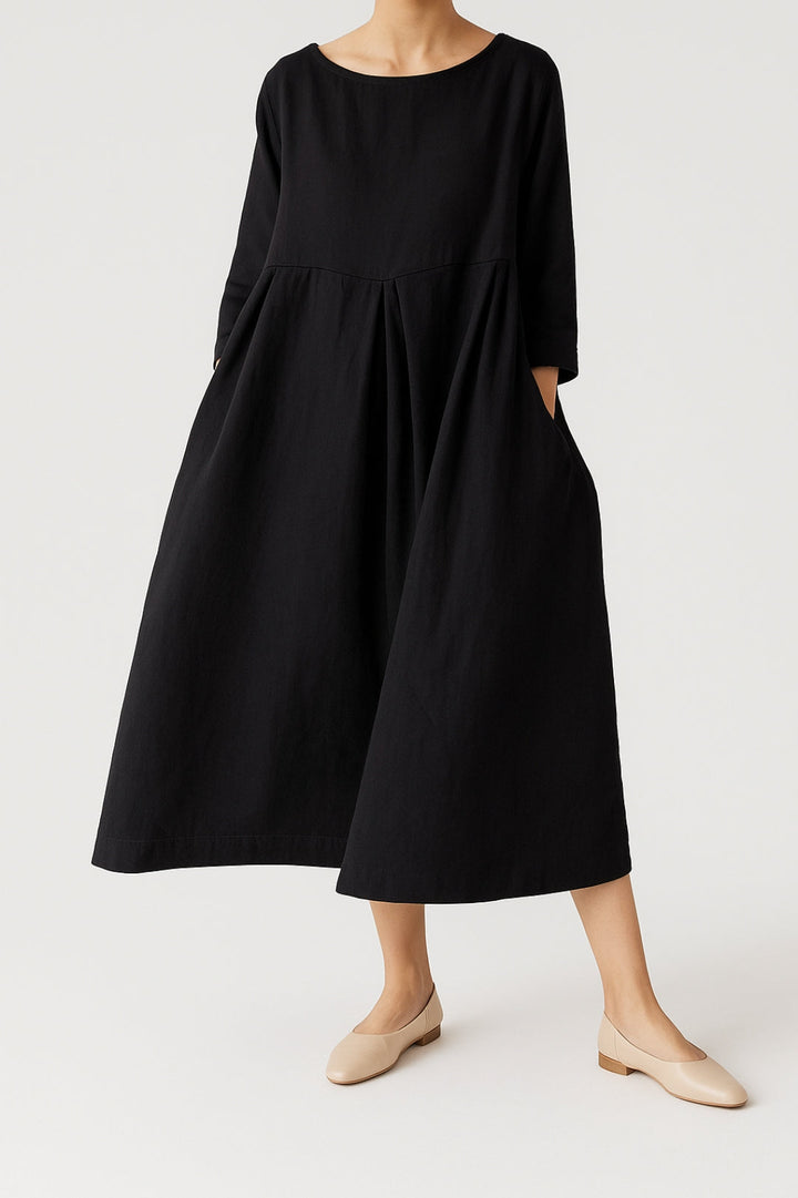Woman dressed in a wide-cut midi dress with soft front pleat detail on a plain background.