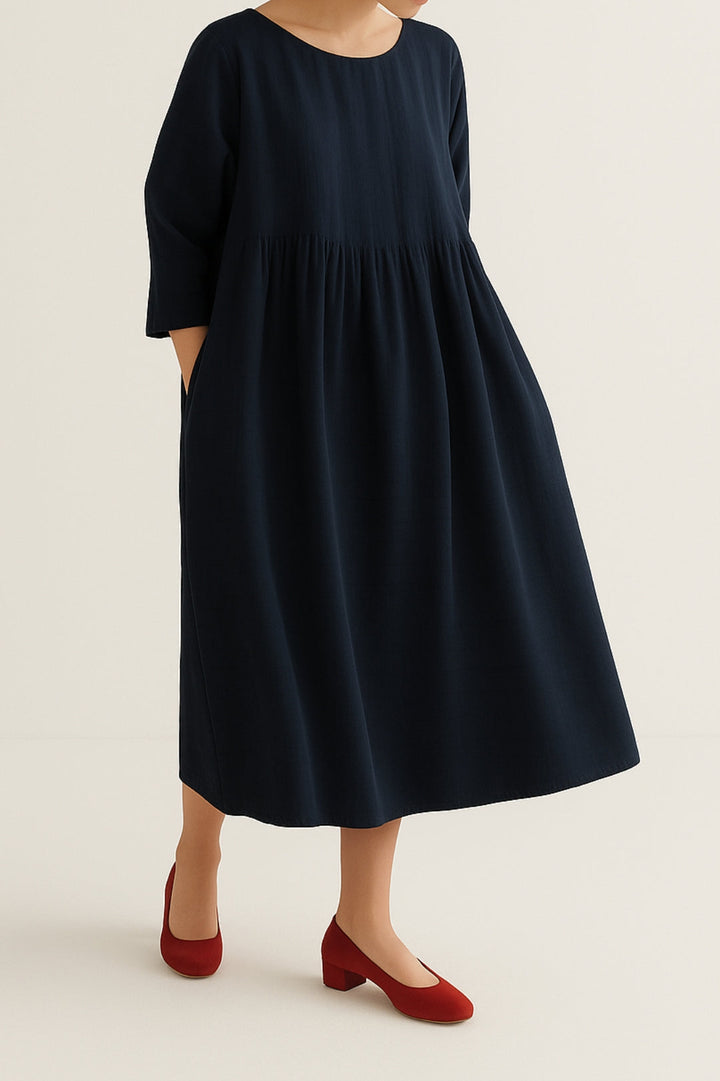 Female model wearing a relaxed fit midi dress with clean drape on a plain background.
