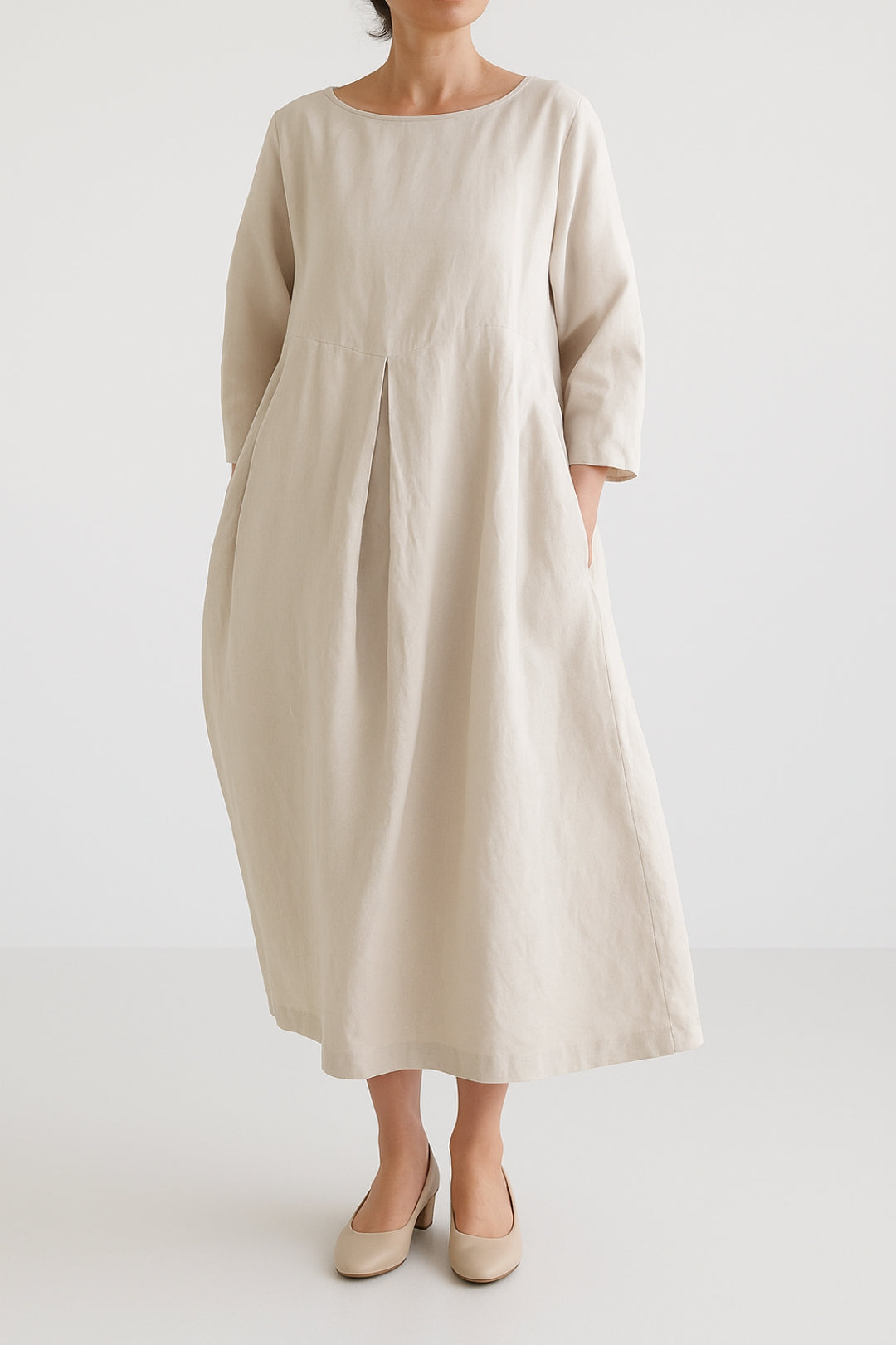Woman showcasing a midi dress with front pleat styling and easy silhouette on a plain background.