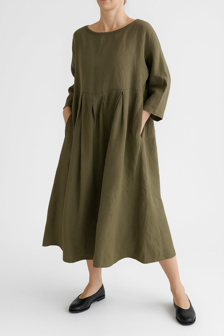 Woman wearing a relaxed midi dress with wide silhouette and front pleat on a plain background.