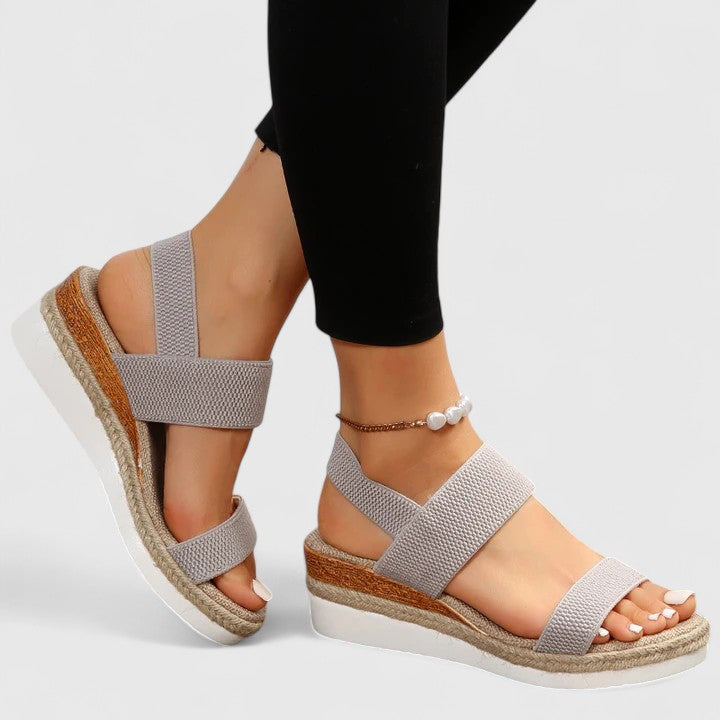  Female wearing open toe sandals with a wedge heel on a plain background.