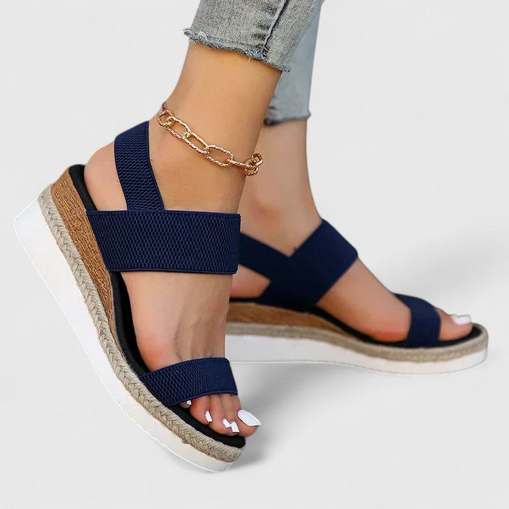 Woman wearing stylish summer wedge sandals on a plain background.